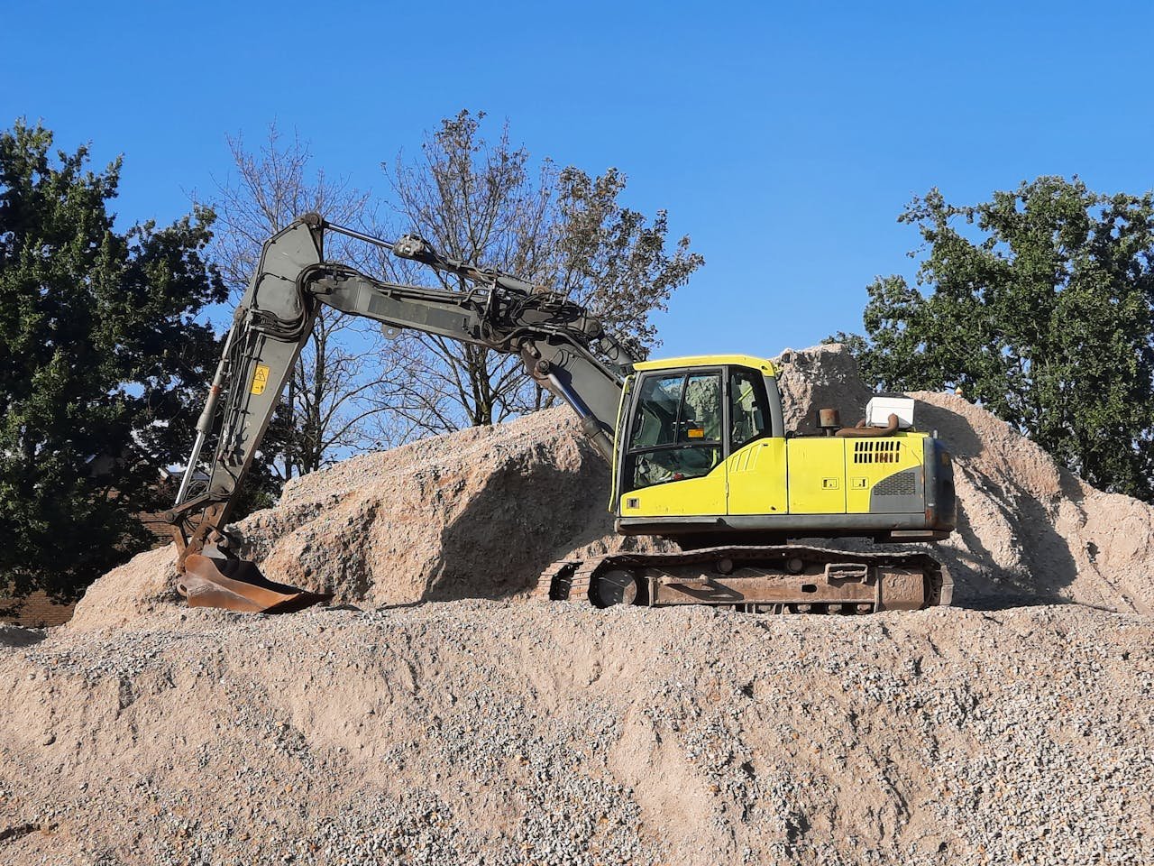 Home A yellow excavator working on a gravel mound at a construction site.
